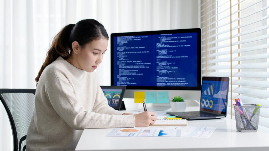 Asia young business woman sit busy at home office desk work code on desktop